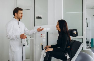 Genç bir kadın fizyoterapistle teşhis makinesinde omurga muayenesi yapıyor..