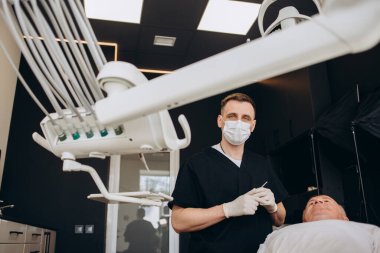 Yetişkin hastaların dişleri üzerinde çalışırken diş matkabı kullanan erkek dişçi.