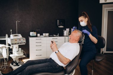 Yakın plan trikoloğu saç büyütme kliniğinde saç dökülmesi olan kel ve olgun bir adamı ve kelleşen erkekler için yaşlanma karşıtı tedavileri tedavi ediyor. Erkekler için saç nakli prosedürleri konsepti, seçici odaklanma.