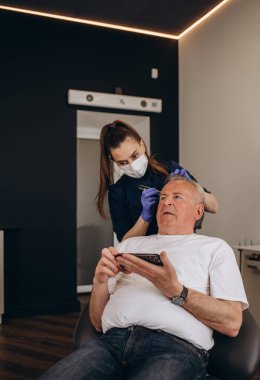Yakın plan trikoloğu saç büyütme kliniğinde saç dökülmesi olan kel ve olgun bir adamı ve kelleşen erkekler için yaşlanma karşıtı tedavileri tedavi ediyor. Erkekler için saç nakli prosedürleri konsepti, seçici odaklanma.