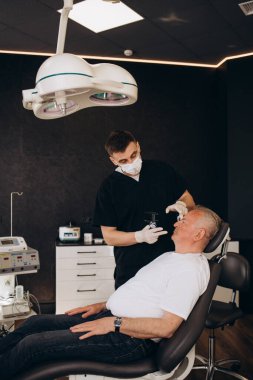 Estetik cerrah yaşlı, gri saçlı bir adamı muayene eder..