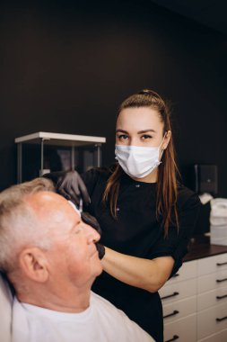 Kaplıca salonundaki olgun bir erkek müşteriye yakın çekim. Profesyonel güzellik tedavisi görüyor. Pamuk pedlerle tanınmaz hale gelen kadın güzellik uzmanı. Deri bakımı konsepti. Erkeksi güzellik..