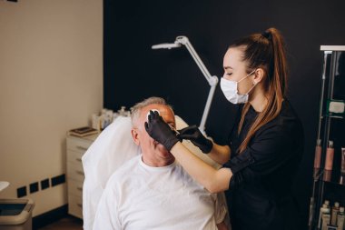 Kaplıca salonundaki olgun bir erkek müşteriye yakın çekim. Profesyonel güzellik tedavisi görüyor. Pamuk pedlerle tanınmaz hale gelen kadın güzellik uzmanı. Deri bakımı konsepti. Erkeksi güzellik..