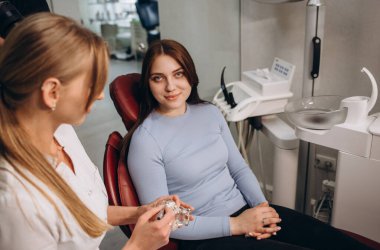 beautiful female dentist holds a model of the jaw and teeth in her hands on which she explains the structure to a girl patient. oral hygiene an example of a jaw in plastic. teeth layout