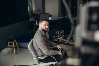 Kafasında kulaklıklarla gülümseyen ve el kol hareketi yapan radyo istasyonundaki stüdyo mikrofonundan gazeteye haberler okuyan bir radyo sunucusu.