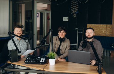 Yayın stüdyosunda podcast yapan iki radyo sunucusunun yan görüntüsü. İki neşeli radyo sunucusu stüdyoda podcast kaydediyor. Kayıt ses konsepti yapma teknolojisi.