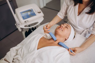 A doctor cosmetologist makes a microcurrent facial therapy to a young woman with a device in a beauty wellness salon.Cosmetology and professional skin care.