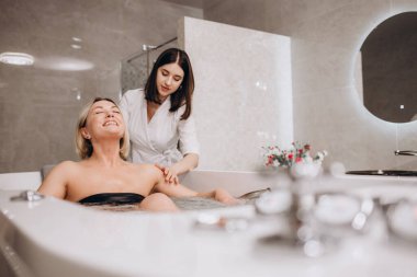 Güzellik salonunda hidromasaj yaparken genç bir kadın. Vücut bakımı ve kaplıca kavramı. Masöz, banyodaki kıza su püskürterek masaj yapar.