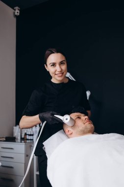 Güzellik uzmanı, güzellik salonunda bir adama kriyoterapi uygular.