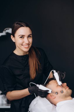 Mikroakım terapisi yakın çekim. Kozmetik uzmanının elleri, erkek yüzü