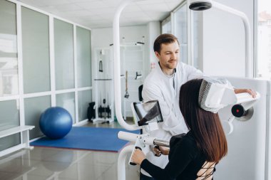 Genç bir kadın fizyoterapistle teşhis makinesinde omurga muayenesi yapıyor.