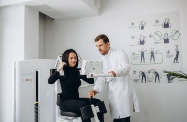 Genç bir kadın fizyoterapistle teşhis makinesinde omurga muayenesi yapıyor.