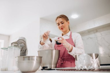 Genç bayan pasta şefi kaynayan şuruba fıstık ezmesi ekliyor. Profesyonel bir mutfakta tatlı pişirmek..