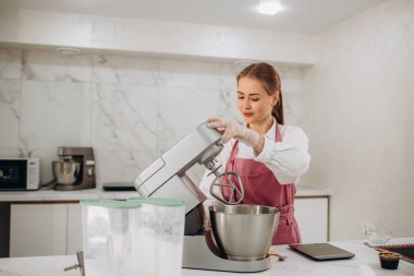 Genç bir kadın pasta için çırpıcı ve krem şanti kullanır, modern mutfakta durur.