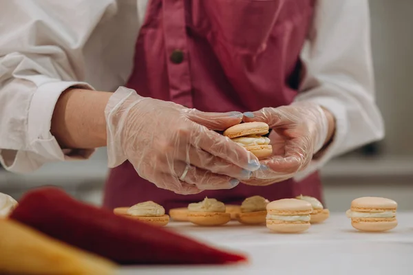 cooking, baking and people concept - chef with confectionery bag squeezing macaron batter or meringue cream to parchment paper at pastry shop kitchen.