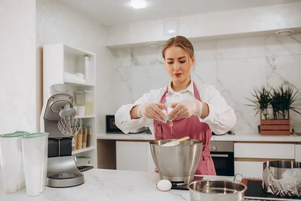 Молодая Женщина Фартуке Разбивает Яйца Тесто Современной Кухне — стоковое фото