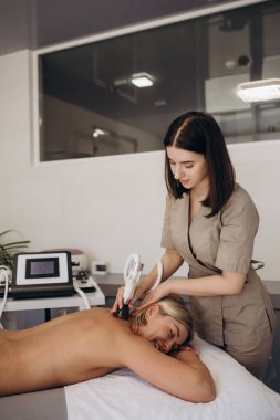 Spa salonundaki kız sırt ve boyun masajı yaptırıyor, kozmetoloji masasında uzanıyor, rahatlıyor ve bu süreçten zevk alıyor.