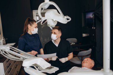 Mutlu ve gülümseme kıdemli adam 70-75 yaşında beyaz dişleri ile bir diş hekimi gözden geçirilmesi, sandalye diş kliniğinde oturan. Genç dişçi doktoruna bakıyorum. Yaşlılar için diş bakımı. Sağlık kavramı