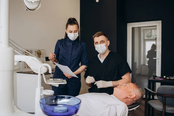 Handsome old man talking to the dentist. Female doctor and senior man in the dentist\'s office. Grandfather looking into the mirror on his teeth. Stock photo