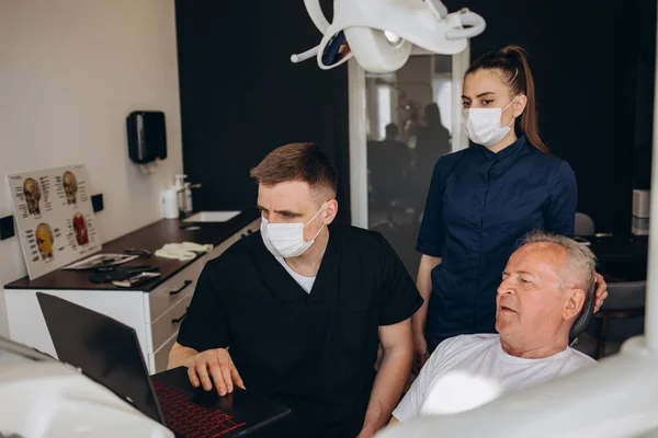 Handsome old man talking to the dentist. Female doctor and senior man in the dentist\'s office. Grandfather looking into the mirror on his teeth. Stock photo