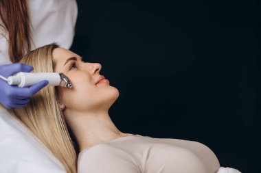 Kozmetik uzmanı bu aleti güzellik salonundaki genç ve güzel bir kadının mikro-akım terapisi için bir prosedür haline getiriyor. Kozmetoloji ve profesyonel cilt bakımı.