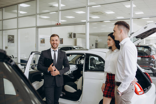Young couple choosing new car for buying in dealership shop.