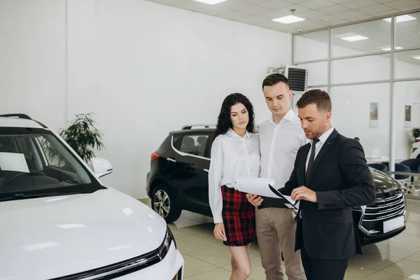 stock image Car dealer showing car to couple in showroom.