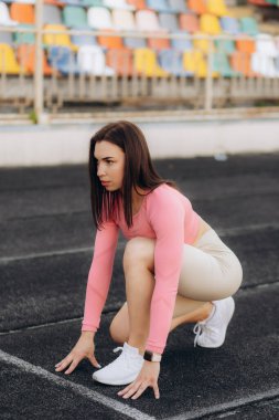 Formda ve kendine güvenen kadın koşmaya hazır. Dişi sporcu gözlerini kaçırarak sürat koşusuna başlamak üzere. Arkadan parlak güneş ışığı