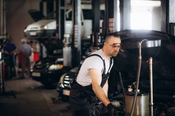 オイル交換のための自動車店で幸せな若い整備士の排水エンジンオイル — ストック写真