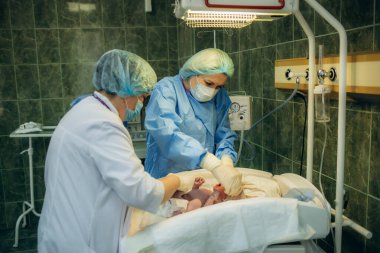 Profesyonel anestezi uzmanı doktor tıbbi ekip ve asistan bebek sezaryeni yapıyor ve bebeği modern hastane ameliyathanesinde doğum ekipmanıyla doğuruyor.