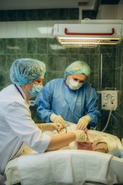 Profesyonel anestezi uzmanı doktor tıbbi ekip ve asistan bebek sezaryeni yapıyor ve bebeği modern hastane ameliyathanesinde doğum ekipmanıyla doğuruyor.