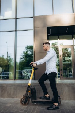 İş toplantısında elektrikli scooter kullanan takım elbiseli genç bir iş adamı. Ekolojik ulaşım kavramı.