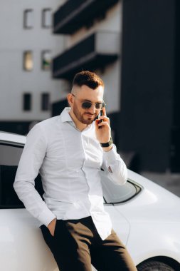 İş adamı, arabanın yanında duran akıllı bir telefonla konuşuyor..