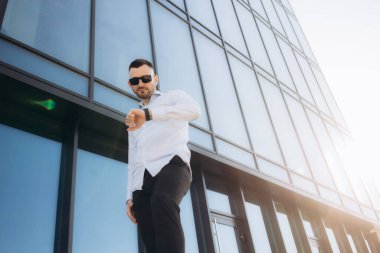 İşadamı evlerin yanında duruyor... erkek portresi binanın arka planında. İş adamı portresi. Adam iş merkezine yakın duruyor. Ofis işçisi. Erkek portresi. Gökdelenlerin yanında bir adam.