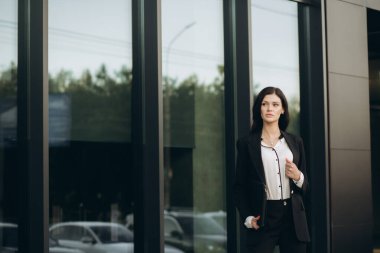 Siyah takım elbiseli genç bir kadın kahve içer ve sokakta dizüstü bilgisayarla poz verir. İş Portresi.