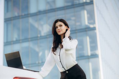 Modern dizüstü bilgisayarını ofis binasının yakınındaki sokakta yürürken kullanan şık bir iş kadını. Gülümseyen kadın serbest yazar tatilde en sevdiği işi yapıyor.