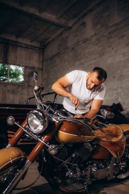 Orta yaşlı bir adam eski motorsikletini garajda tamir ediyor..