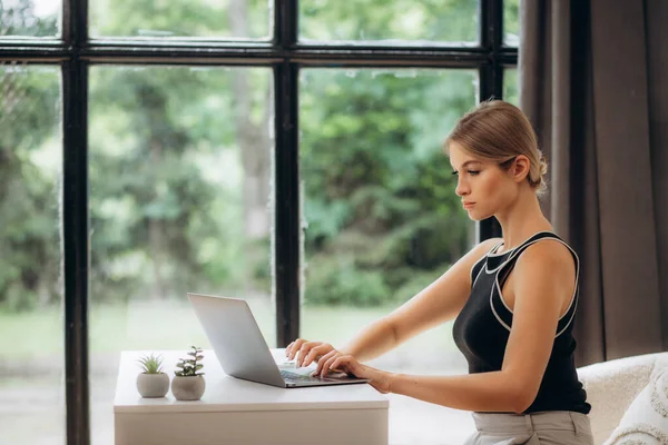 Красива Молода Жінка Працює Ноутбуком Затишному Дивані Біля Великого Вікна — стокове фото