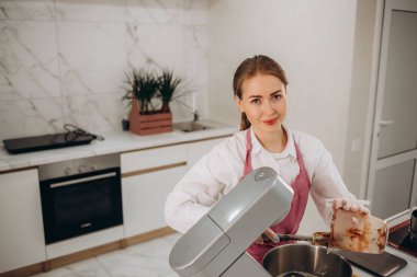 Kadın pasta şefi sünger katmanları ve kremadan pasta yapıyor. Şekerci fırın mutfağında parmak yalıyor pembe krema tadıyor.