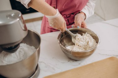 Yemek pişirme, ev işleri, serbest çalışma, insan ve hobi kavramı: Genç kadın pasta şefi kremi karıştırıyor ve tabletteki tarife bakıyor. Modern mutfak..