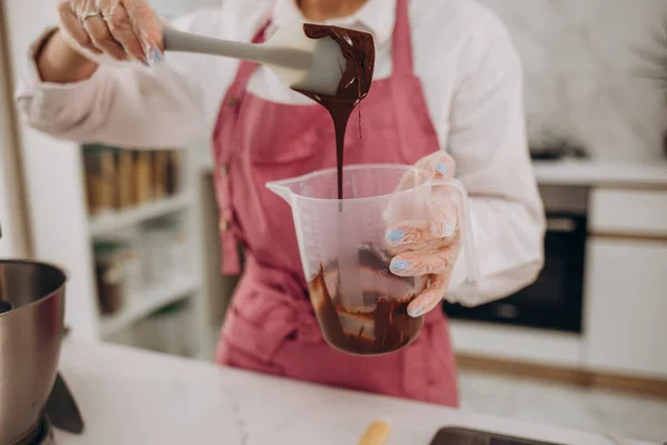スポンジ層とクリームのケーキを作る女性ペストリーシェフ 菓子パン屋キッチンでピンククリームを味わう指をなめる — ストック写真