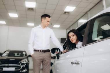 Happy millennial couple taking car key from auto salesman, sitting inside modern automobile at dealership, panorama. Cheery young family buying new vehicle at modern showroom