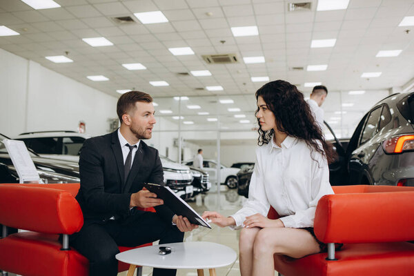Удовлетворенная счастливая белая клиентка клиент женщина сидит за рулем новой машины делает тест-драйв перед покупкой автомобиля в то время как мужчина помощник магазина помогает ей выбрать его