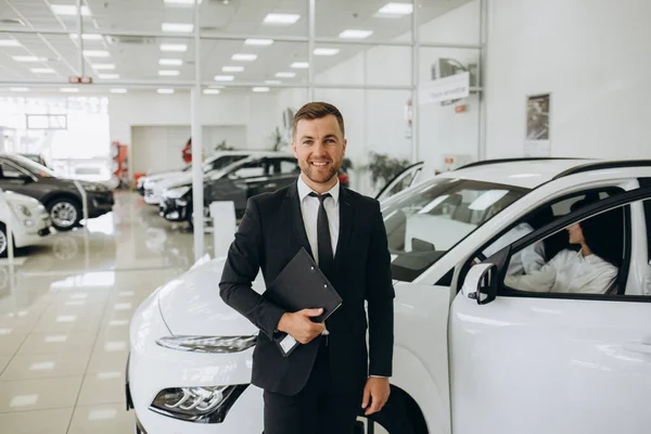 Kendine güveni tam beyaz bir erkek mağaza asistanının resmi kıyafetleriyle otomobil galerisindeki kameraya bakarken yakın plan çekimi.