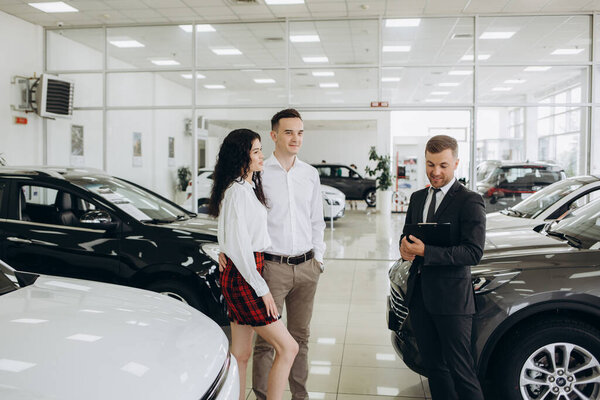Car dealer showing car to couple in showroom.