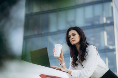 Çekici bir kadın arabasının yanında duruyor. Faiziyle birlikte bir tablet kullanıyor. Hanımefendi gülümsüyor ve neşeyle kameraya bakıyor..