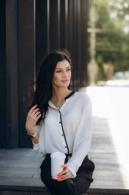 Dizüstü bilgisayar ve belgelerle mola sırasında ofis dışında yürüyen paket kahve fincanı tutan resmi giyim genç zarif kafkas iş kadını düşük açı çekim. İş merkezinde ofis çalışanı