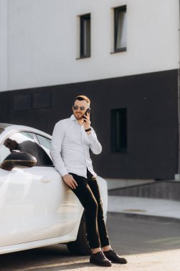 Büyük şehirde arabasının yanında akıllı telefondan konuşan ciddi bir finansal mafya üyesi.