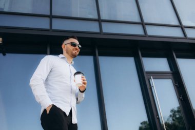 Telefonla gülümseyen Avrupalı işadamı ofis binasının yakınında kahve içiyor..