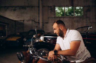 Bir adam garajda motosikletin üstünde oturuyor..